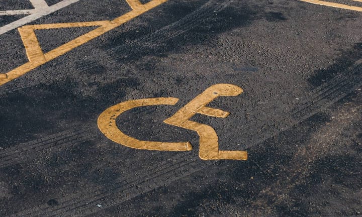 Disabled parking bay, yellow wheelchair sign on tarmac; tyre treads on tarmac visible over the sign