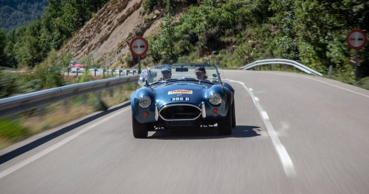 A blue AC cobra photographed from the front, driving along a mountain road