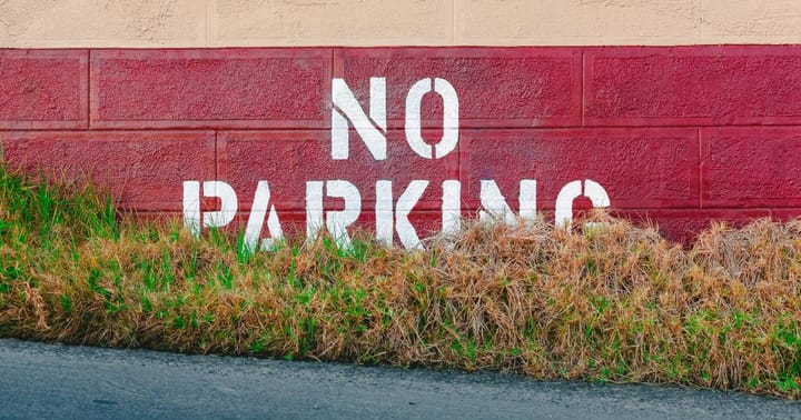 A red wall with the words 'no parking' printed in white paint, fronted by an overgrown grass verge