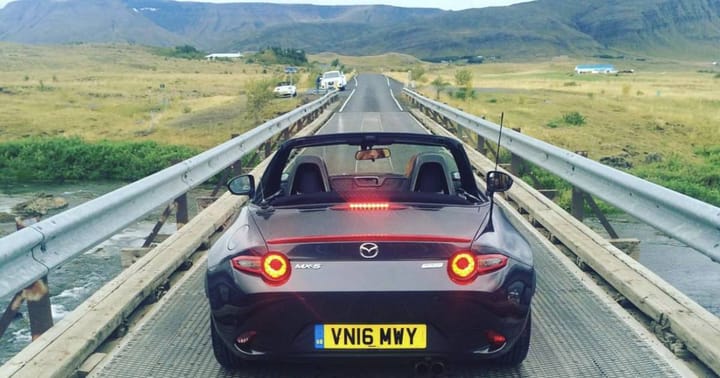 A Mazda MX-5 pictured from the rear on a bridge over a river in Iceland