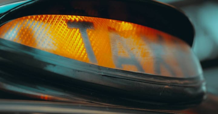 An orange UK taxi sign, the 'i' of taxi almost invisible so the word reads 'tax'